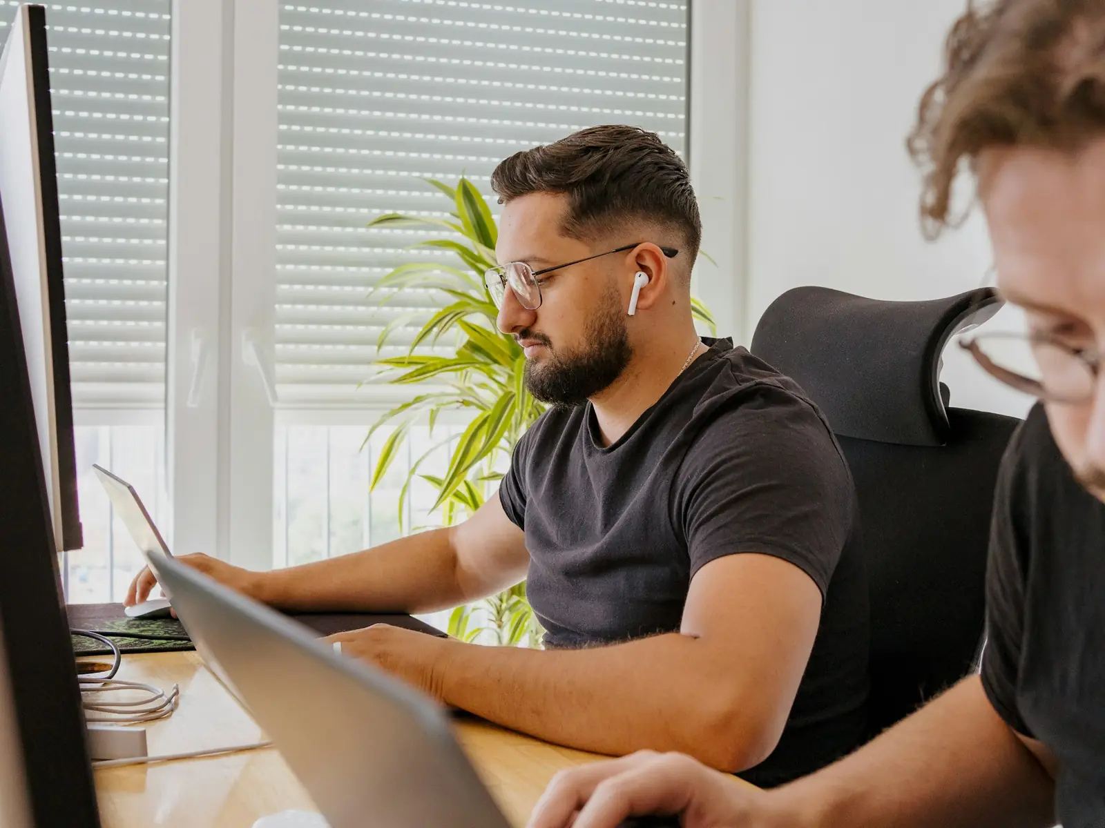 Zwei Kollegen arbeiten nebeneinander an ihren Bildschirmen in einem hellen Büro mit Tageslicht